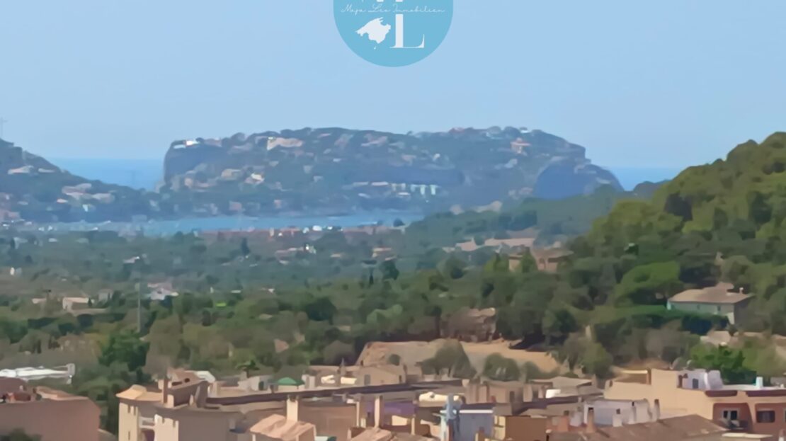 Blick auf eine Landschaft mit Hügeln, Häusern und einem Küstenbereich im Hintergrund.
