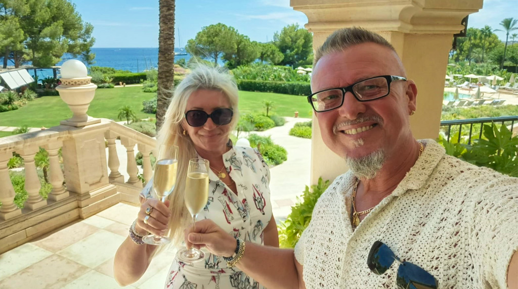 Dwie osoby siedzą przy stole i omawiają dokumenty z widokiem na wybrzeże Majorki. W tle widać przezroczyste ściany i widok.