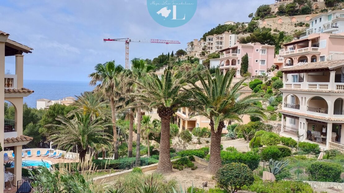 Blick von der überdachten Terrasse mit Holzlamellen auf gepflegte Häuser, grüne Anlage und Meerblick in Port Andratx, Mallorca.