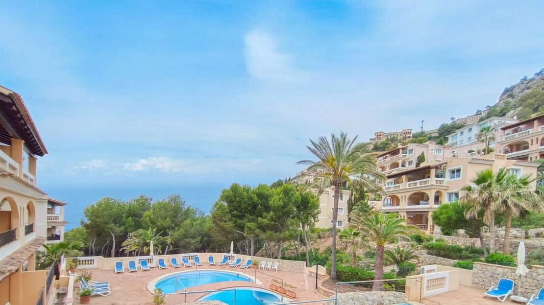 Blauer Himmel über Port Andratx mit Meerblick, Palmen und türkisblauem Pool zwischen mediterranen Wohnhäusern, klarer Horizont.